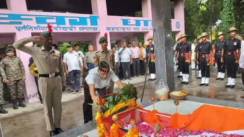 Uniformed personnel salute beside a tricolour-draped body covered in marigold garlands and rose petals at a cremation ground in Bahraich