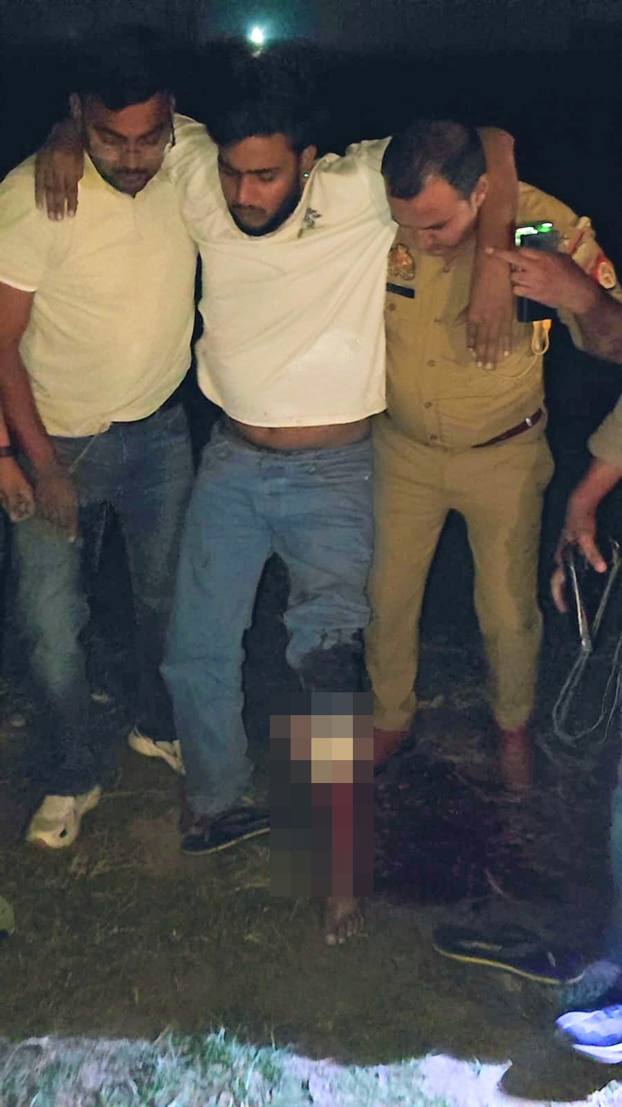 A man is supported by two others; the lower-leg injury area is locally obscured