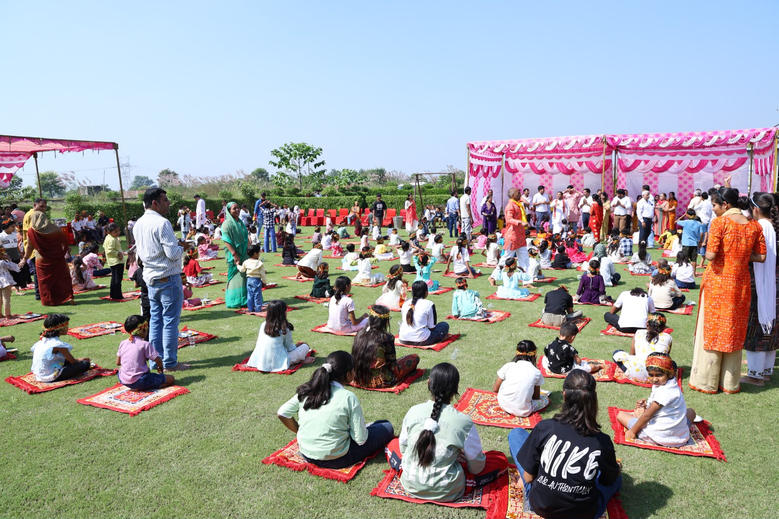 संस्कार उपवन के आयोजन में हरे लॉन पर लाल चटाइयों पर बैठे बच्चे और आसपास उपस्थित वयस्क