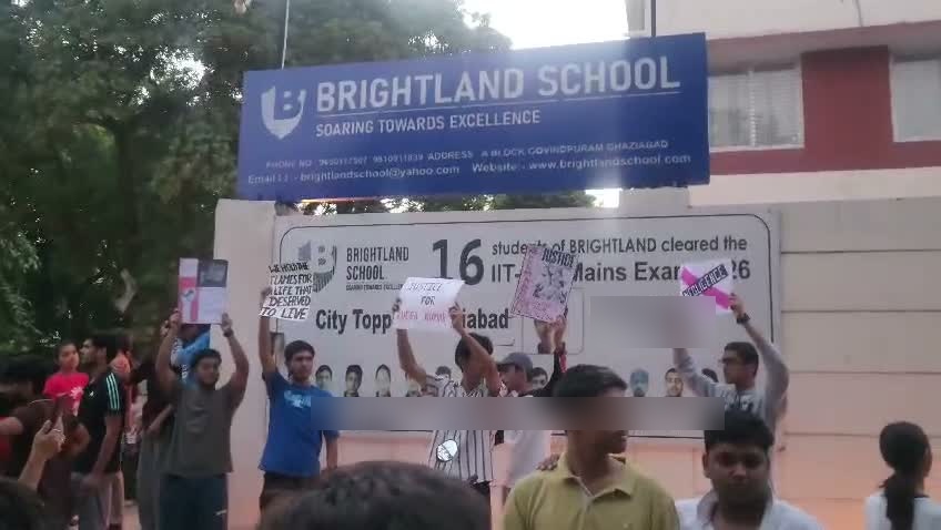 People holding placards gather below the Brightland School sign