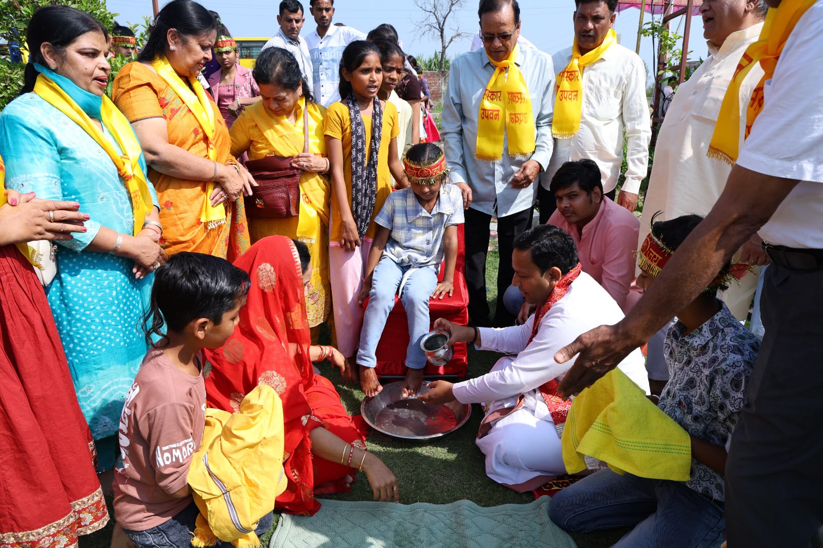 चरण प्रक्षालन के दौरान लाल कुर्सी पर बैठे बच्चे के पैरों के नीचे रखा धातु का पात्र