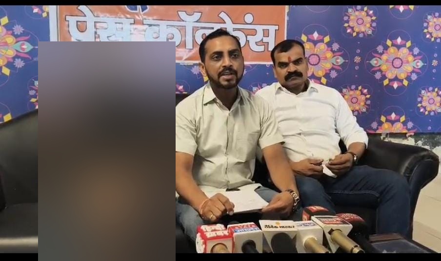 Press conference photograph with the left seated person obscured for privacy