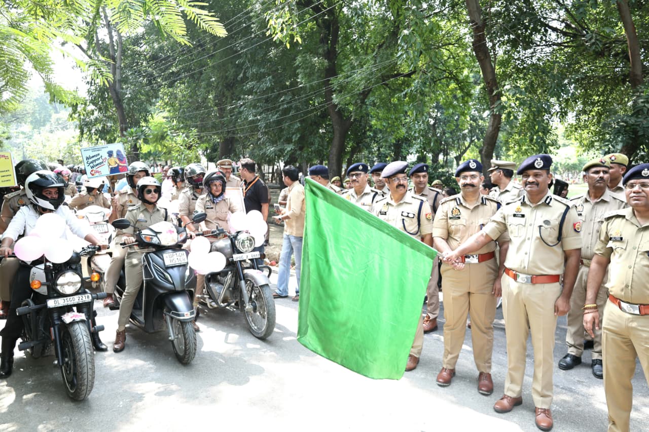 Police officers hold a green flag beside women riders at the rally flag-off
