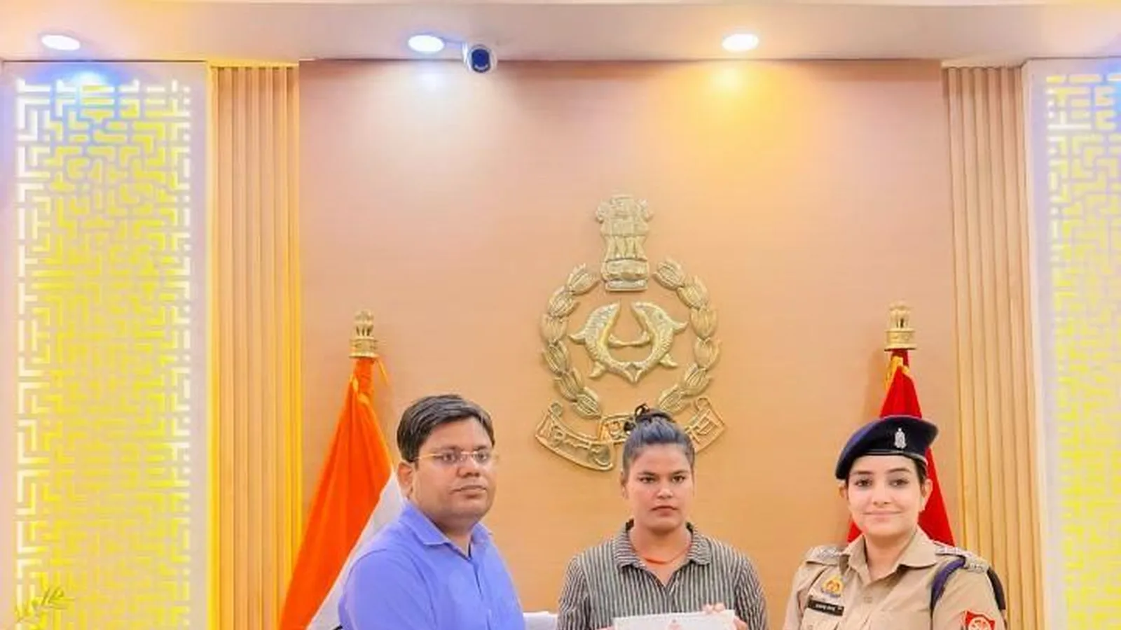 Three people hold a document behind an office desk, including a woman in khaki police uniform