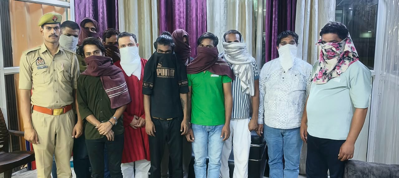 वर्दीधारी पुलिस अधिकारी के साथ खड़े वयस्क पुरुषों की समूह तस्वीर, कई पुरुषों के चेहरे कपड़े से ढके हैं