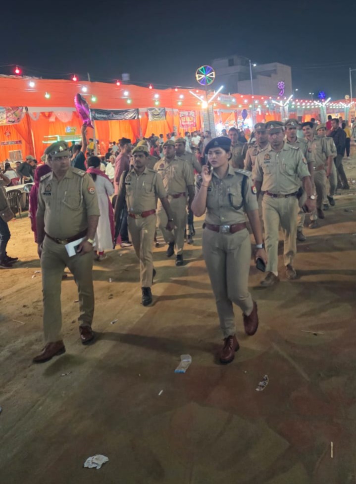 रात में रोशनी से सजे आयोजन परिसर में वायरलेस सेट के साथ आगे चलते अधिकारी और पुलिस टीम