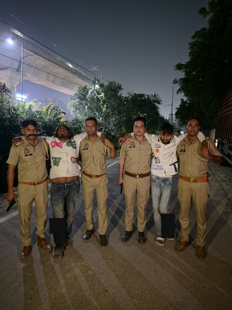 सड़क पर चार पुलिसकर्मियों के साथ दो आरोपी, जिनके पैरों पर संपादकीय मास्क लगाए गए हैं।