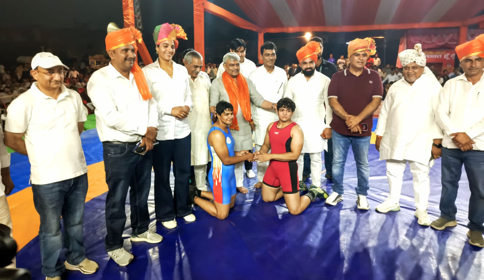 तंबू के नीचे आमने-सामने बैठे दो पहलवान हाथ मिलाते हुए
