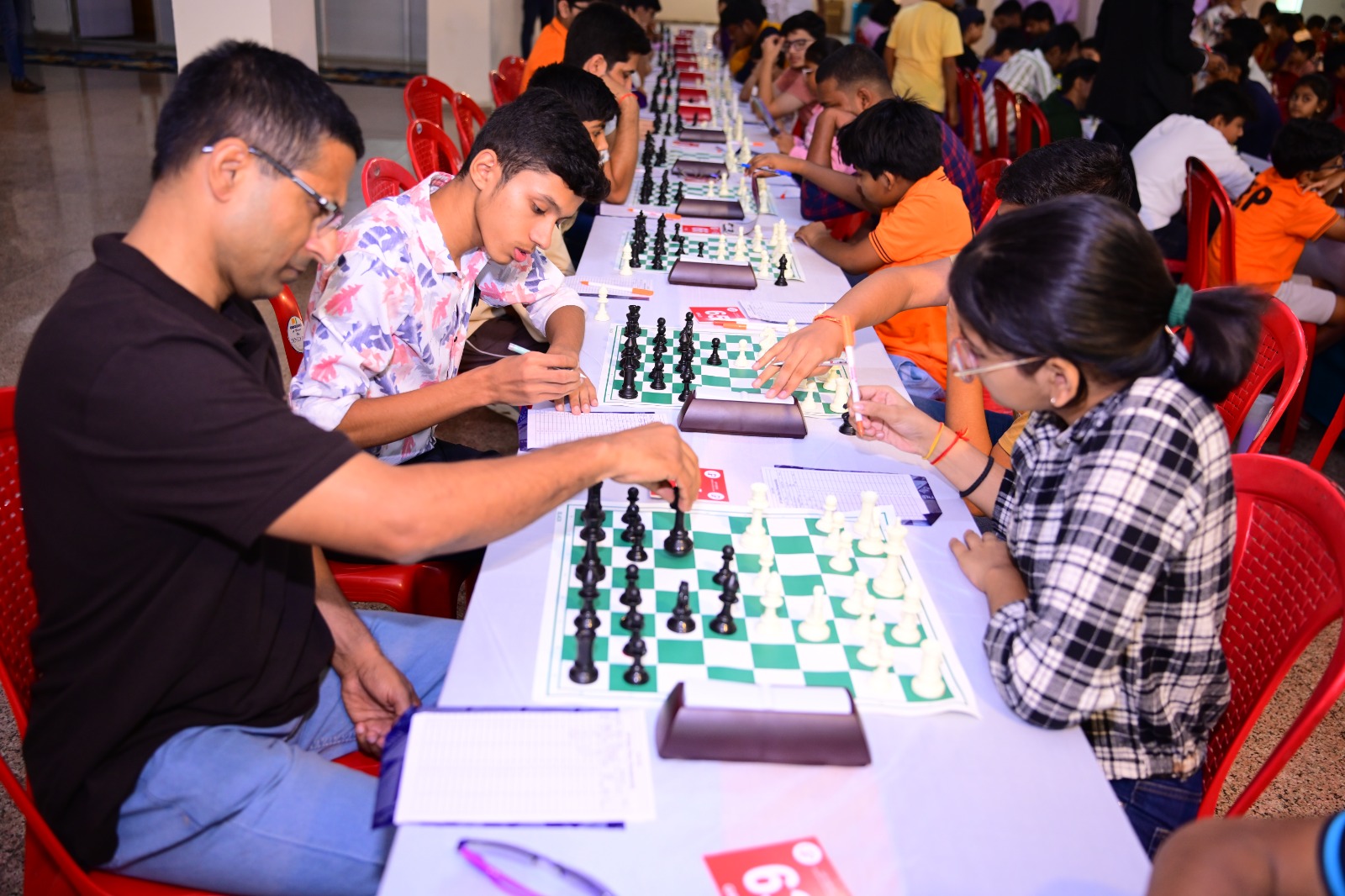 मेज पर शतरंज बोर्ड और घड़ियों के साथ खेलते प्रतिभागी।