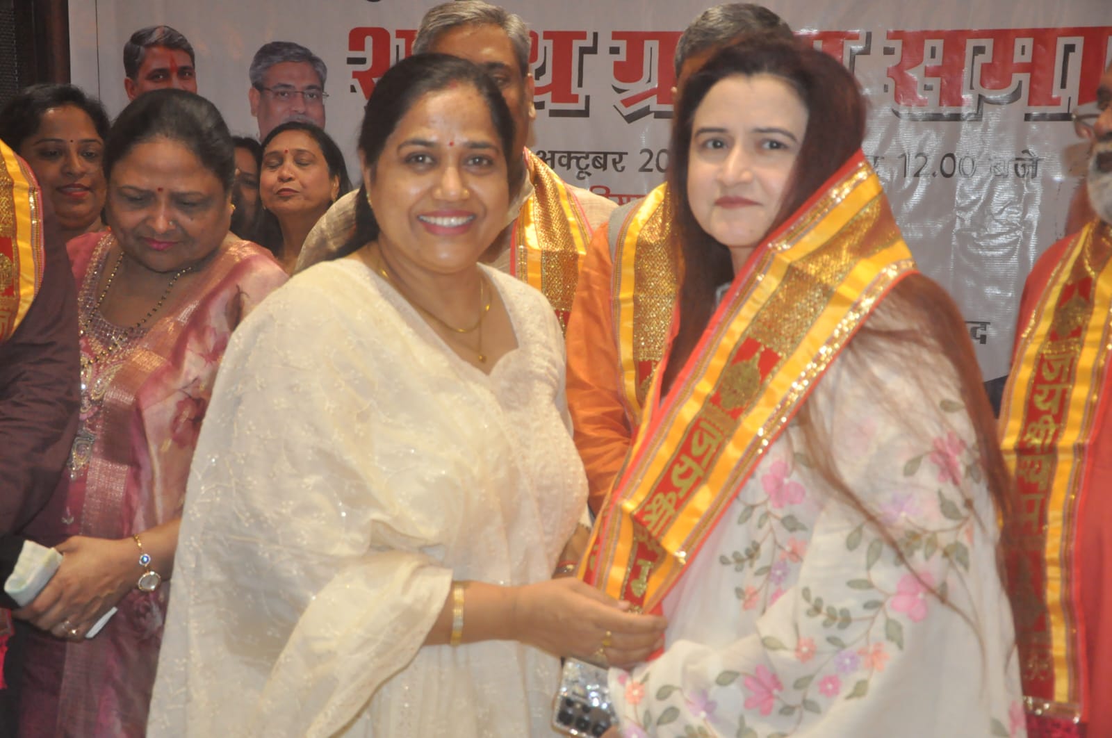 Two participants at the ceremony; the background banner shows October and 12.00.